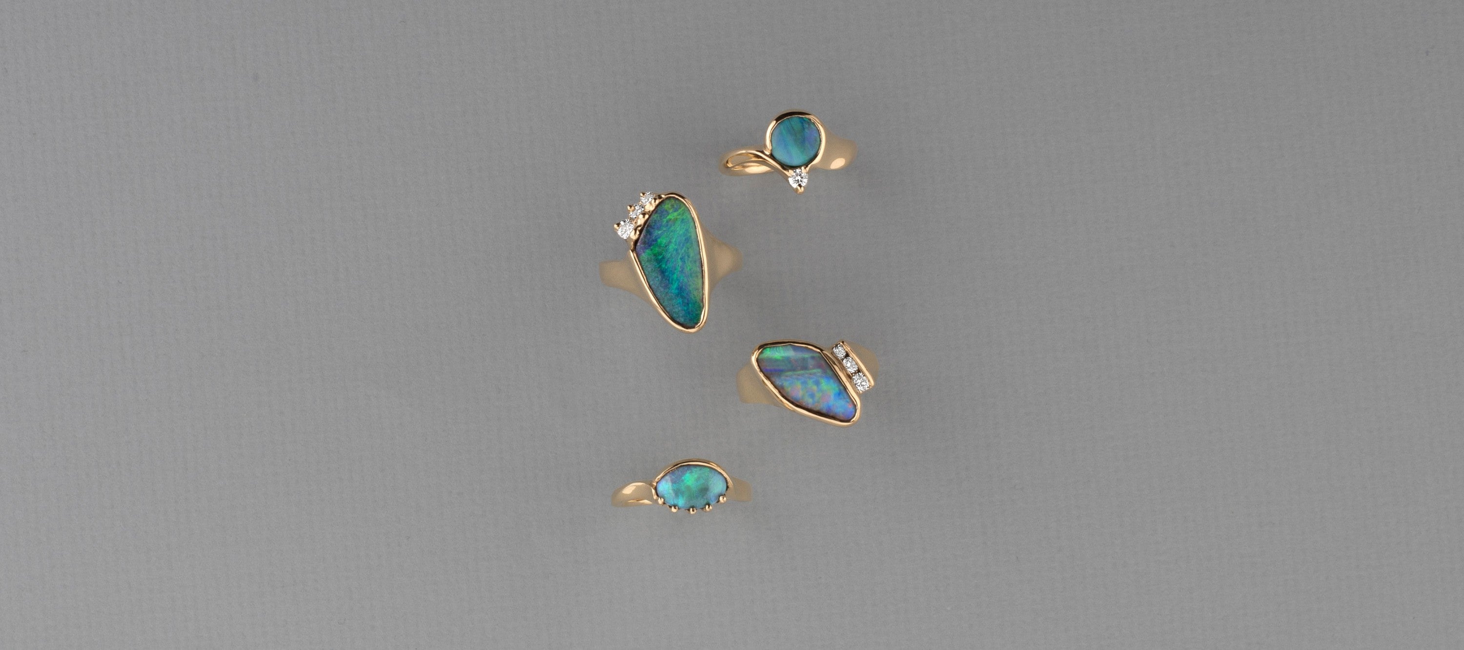 Four gold and opal rings designed by deJonghe Jewelry on a gray background