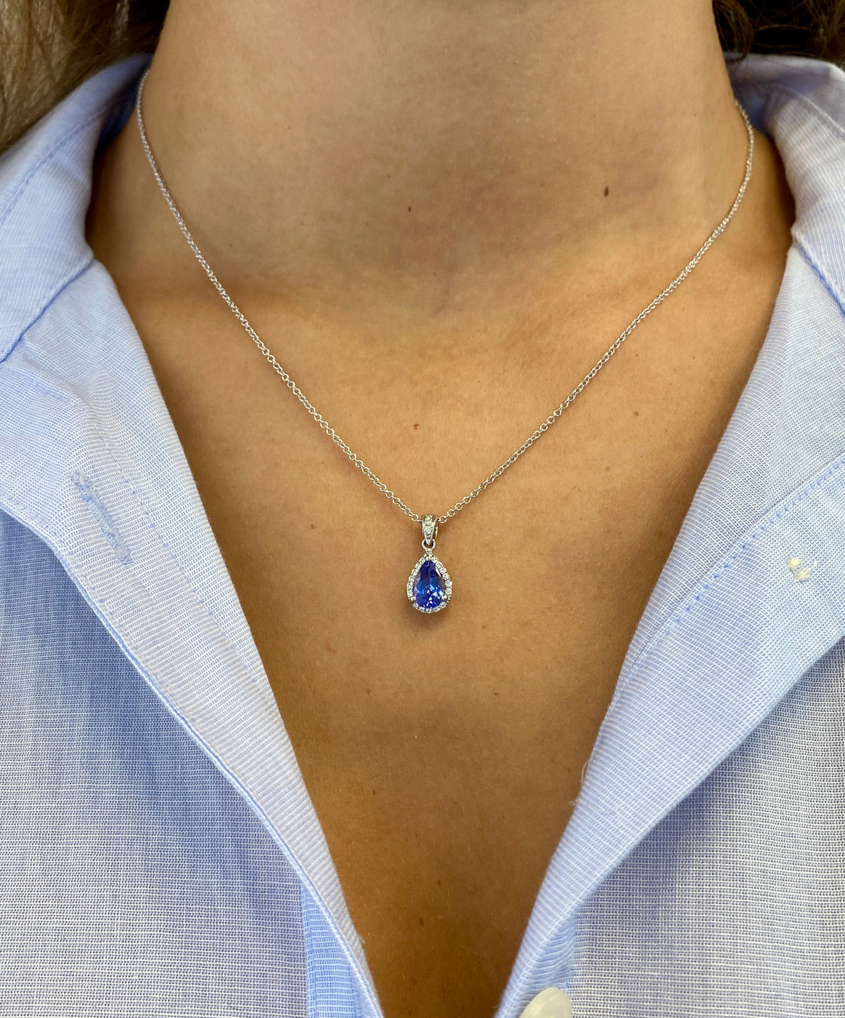 14k white gold necklace with pear-shaped tanzanite center stone, round diamond halo, and diamond-set tapered bail