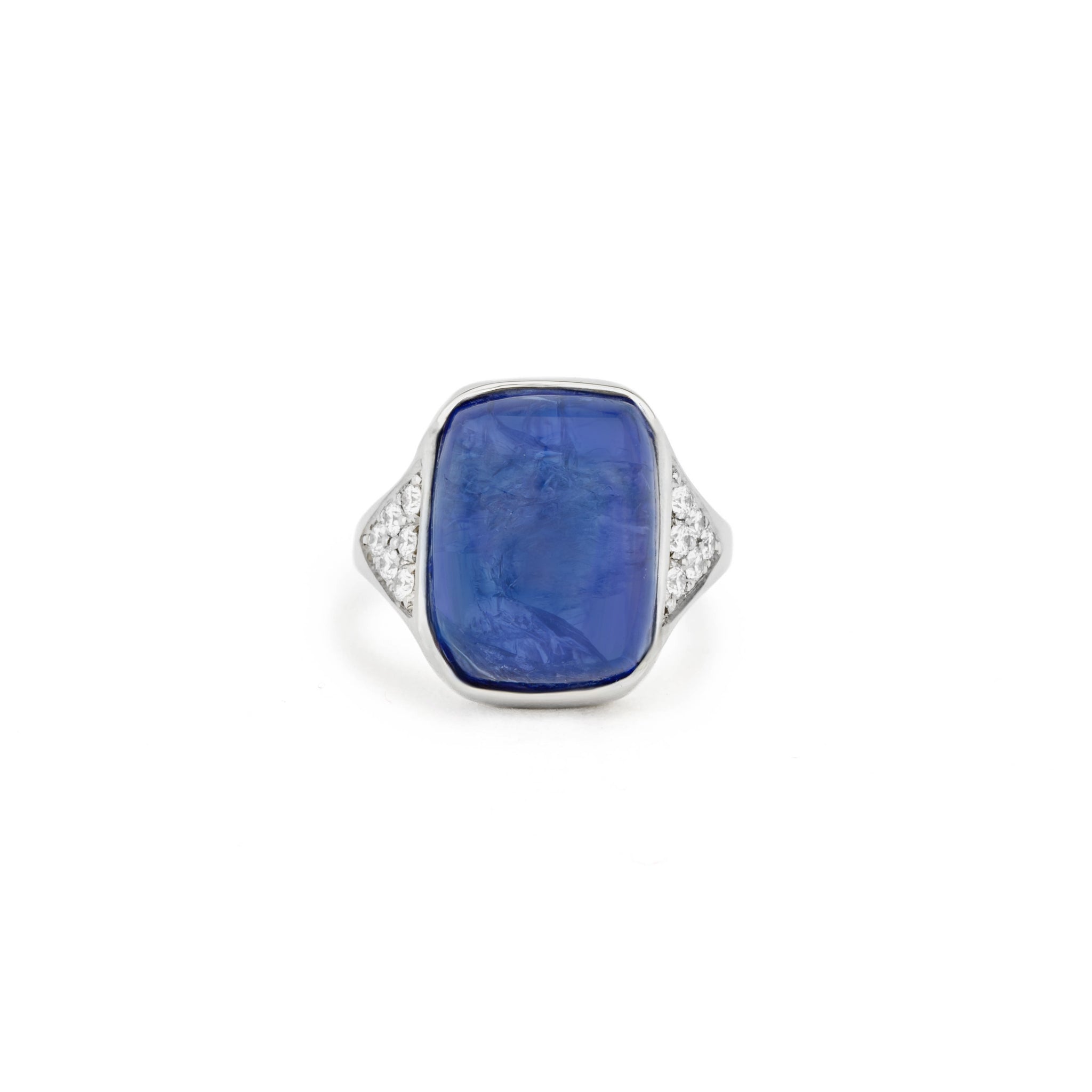 White gold ring with a large cabochon tanzanite in a hand-carved setting, flanked by pavé set diamond