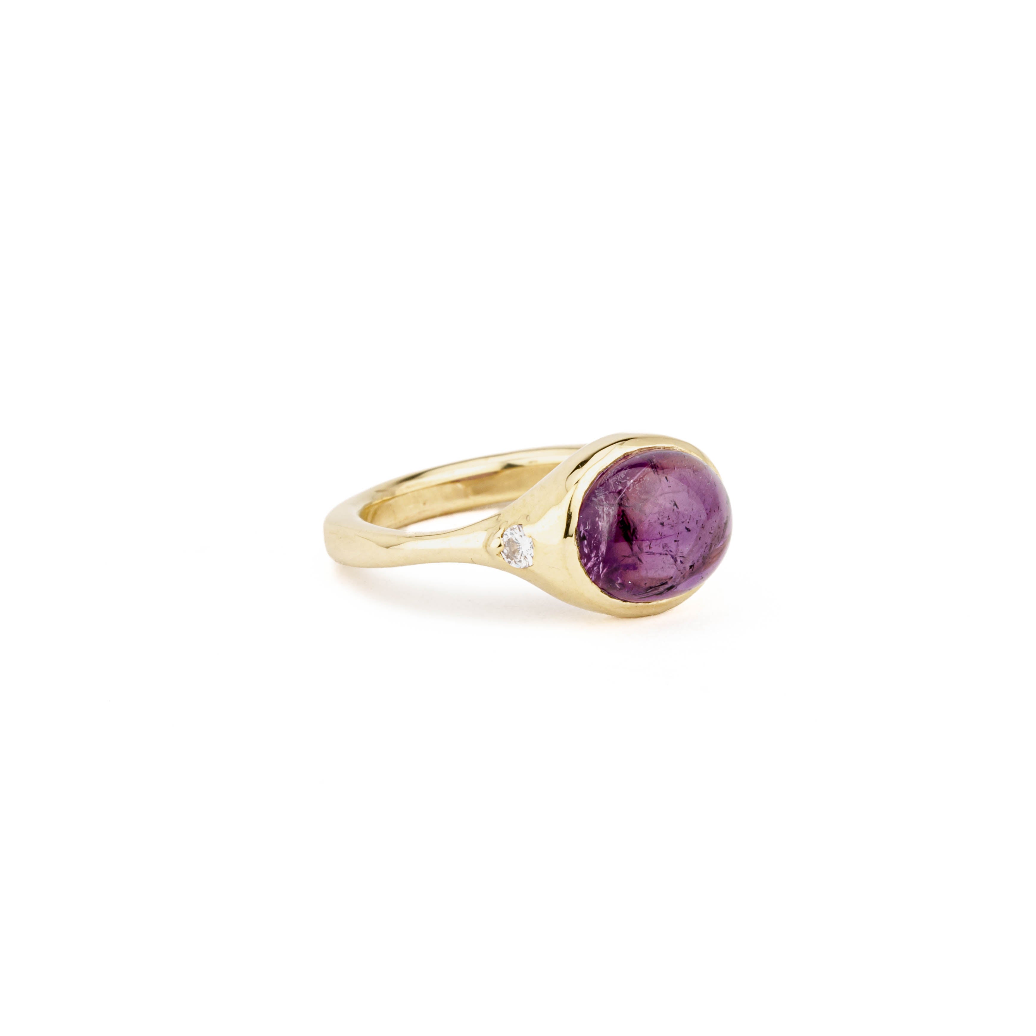 14k yellow gold ring with an oval amethyst cabochon bezel set at center, flanked by two flush-set round diamonds on a split shank with square bottom.