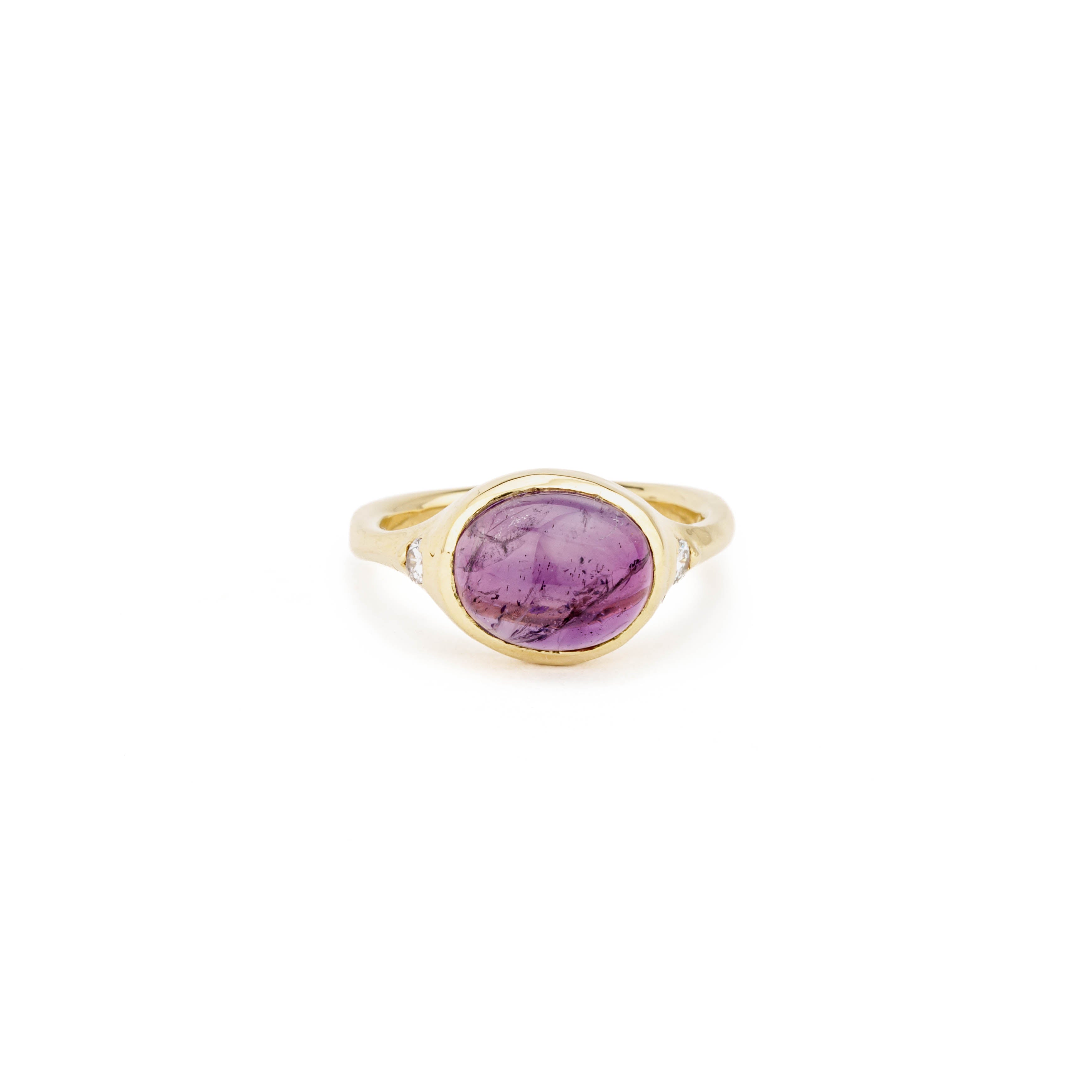 14k yellow gold ring with an oval amethyst cabochon bezel set at center, flanked by two flush-set round diamonds on a split shank with square bottom.