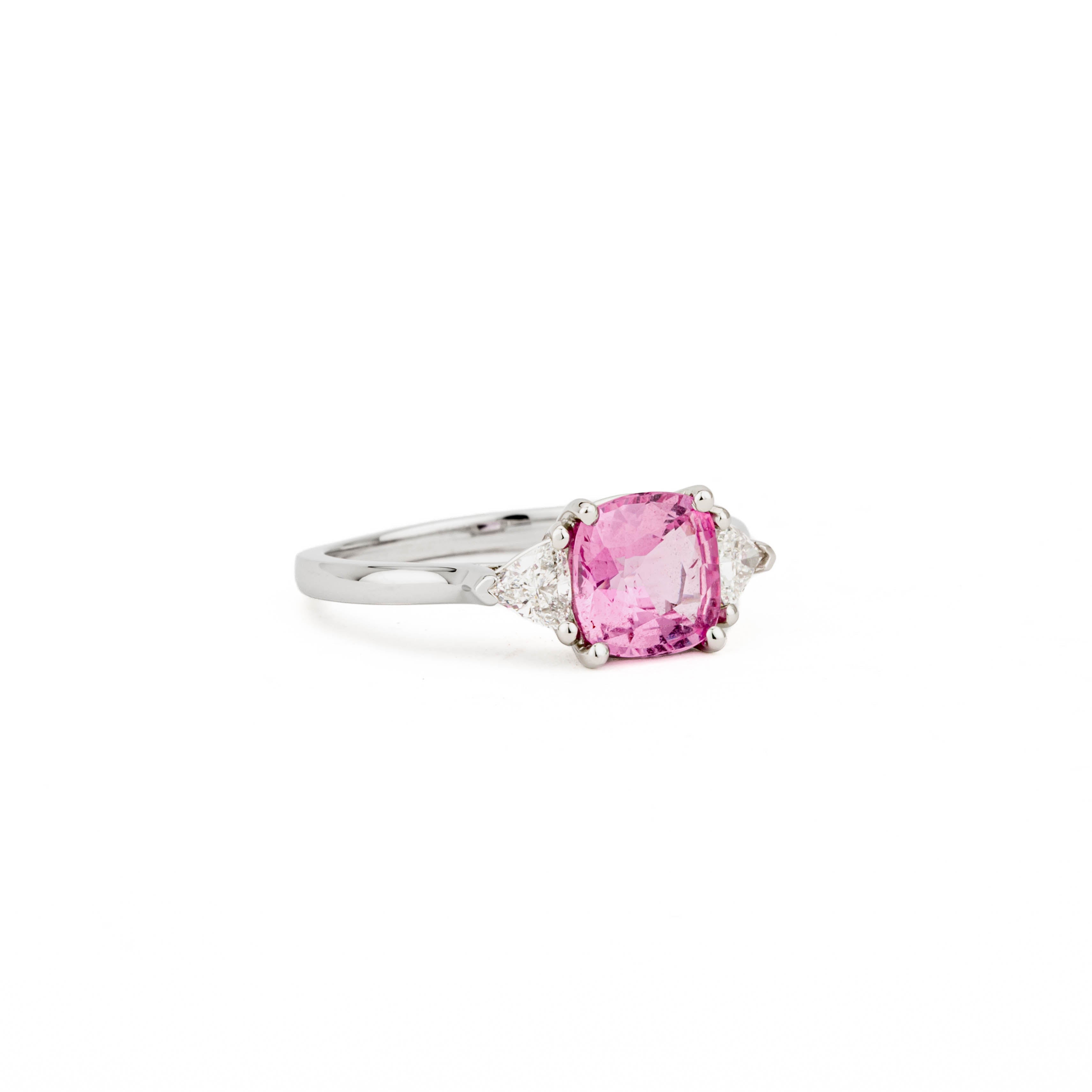 Platinum three-stone ring with cushion cut pink sapphire center stone and trillion cut diamond side stones