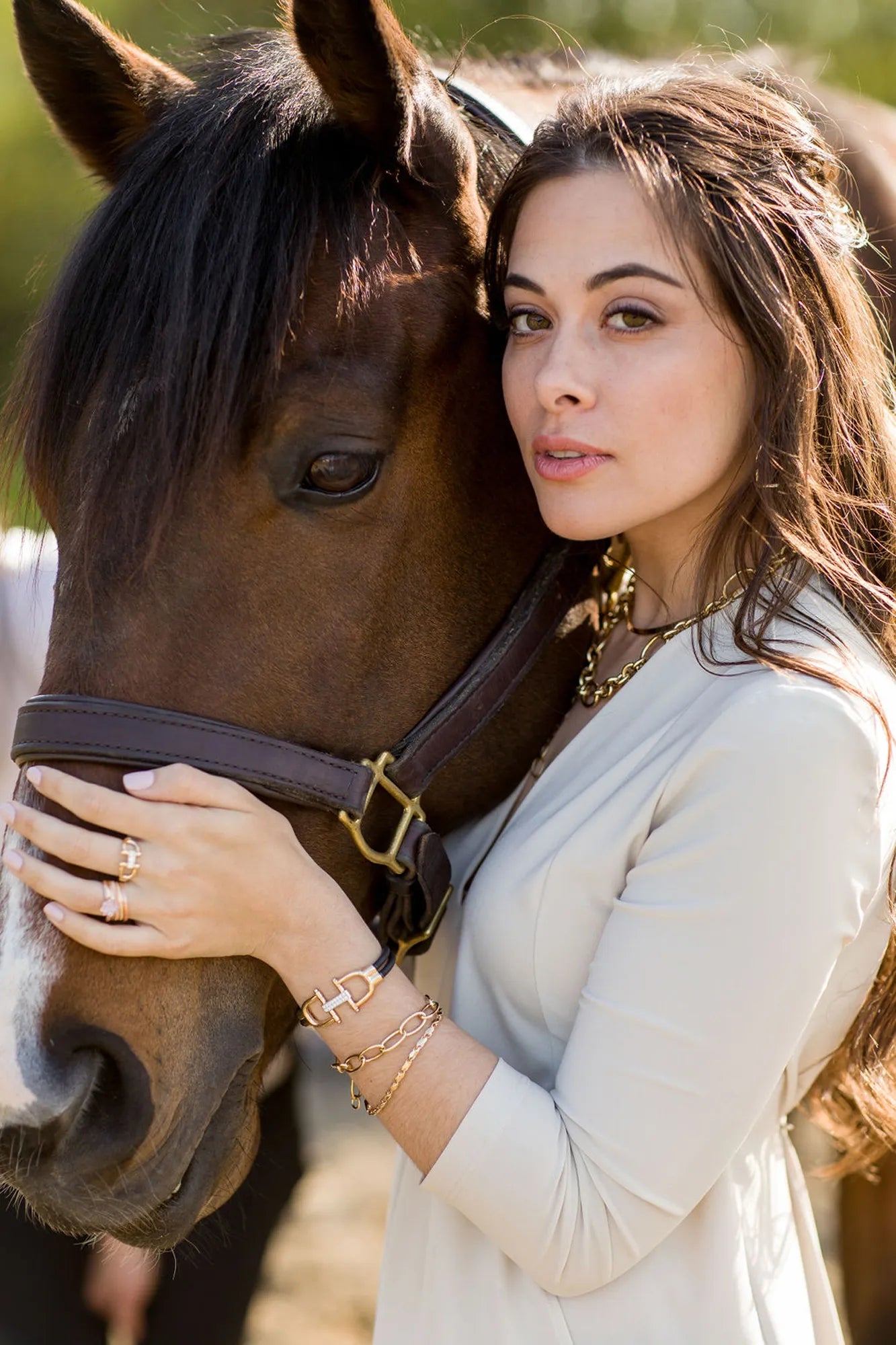 Girl holding a horse wearing a snaffle bit bracelet in 14k yellow gold, a snaffle bit ring in 14k yellow gold, and other gold jewelry. 