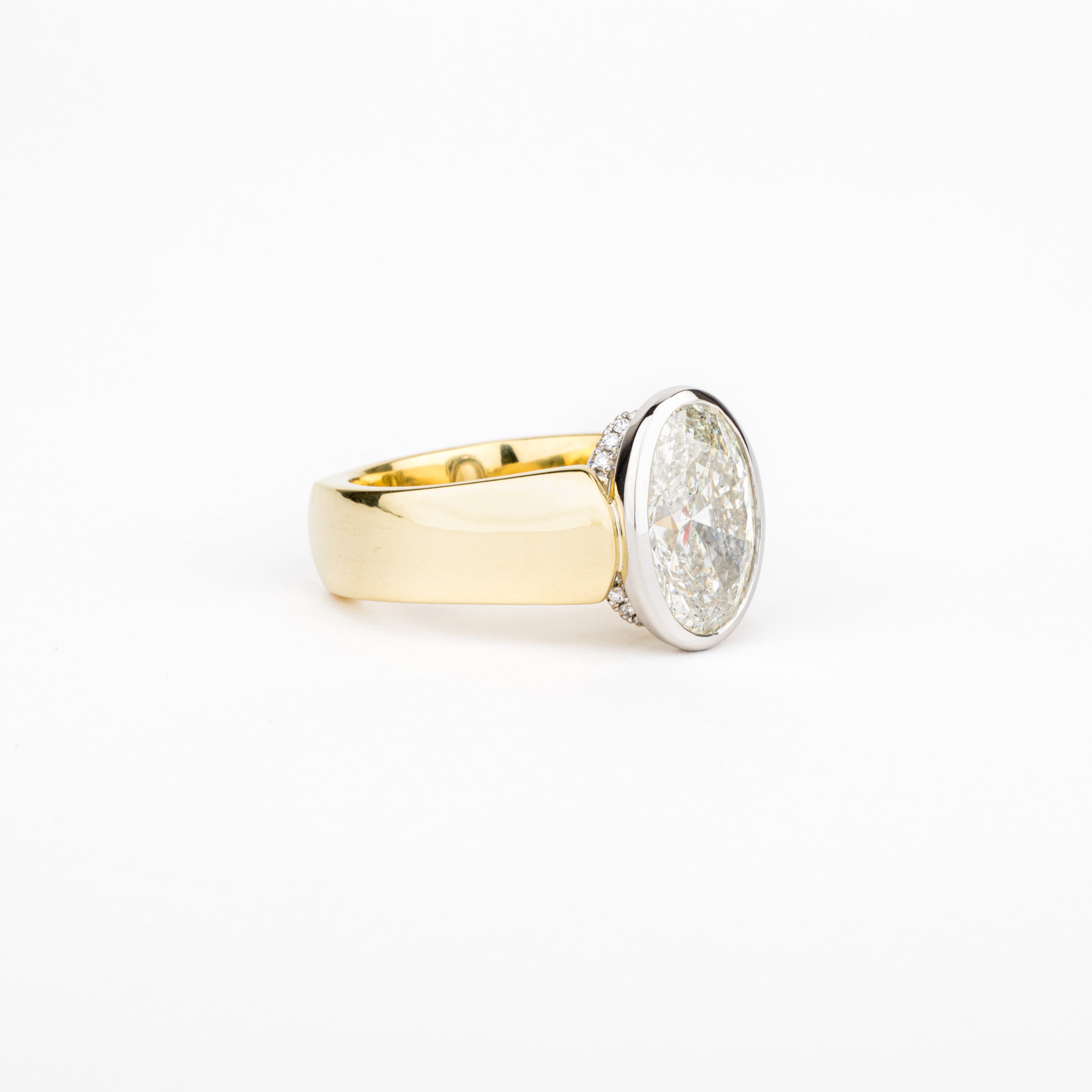 Custom oval diamond engagement ring in yellow gold with an oval diamond set in a bezel and a hidden halo