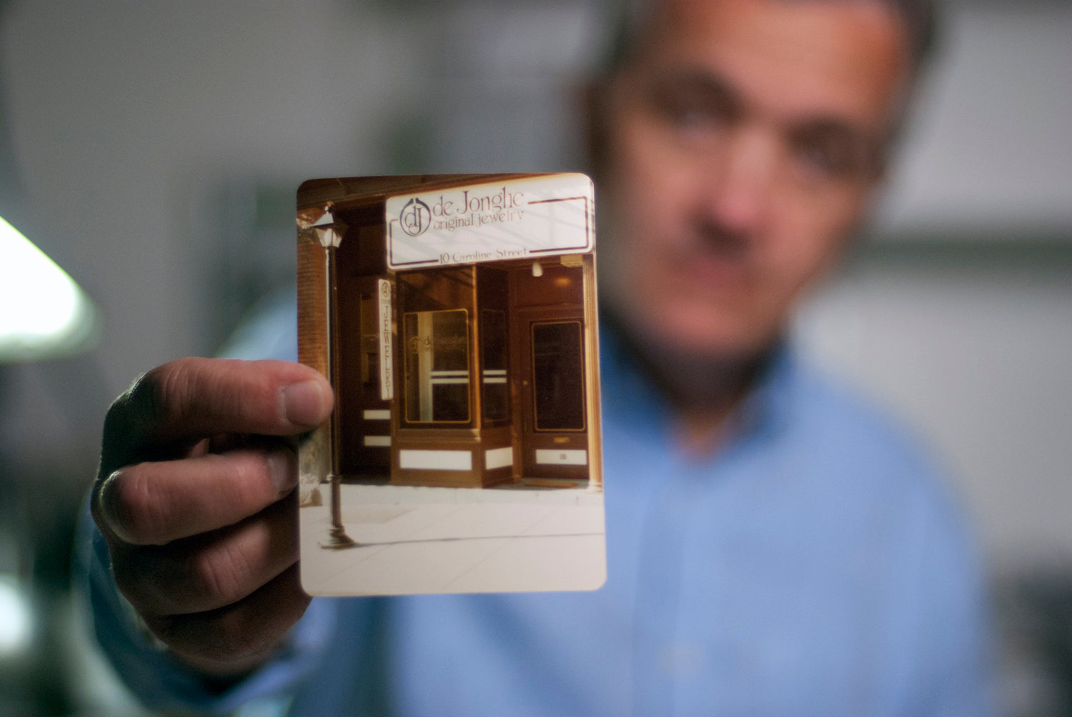 Dennis deJonghe holding a photograph of his first storefront of deJonghe Original Jewelry on Caroline St. in Saratoga Springs, NY. 