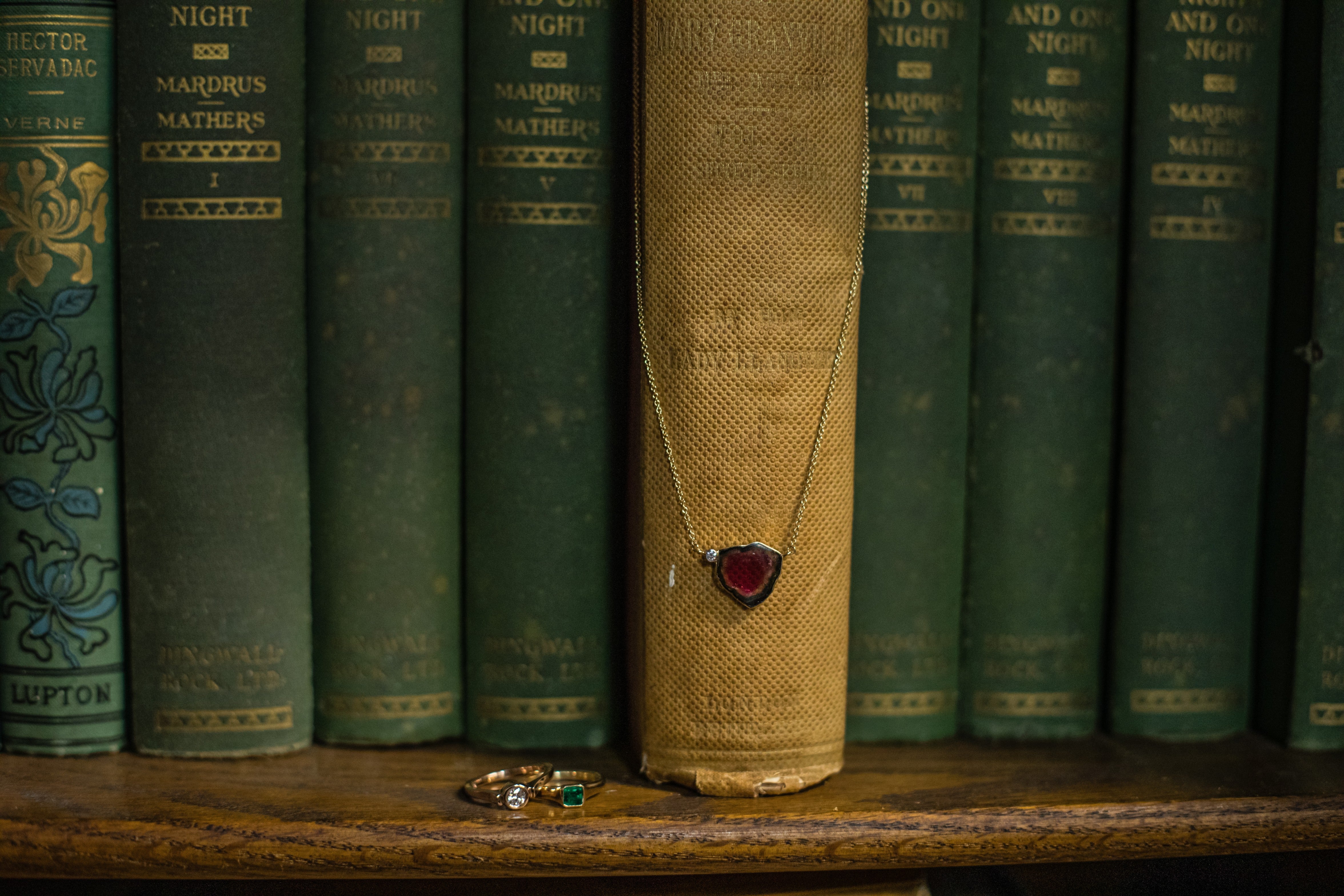 Vintage books with a watermelon tourmaline necklace from deJonghe Original Jewelry and rings on a wooden surface