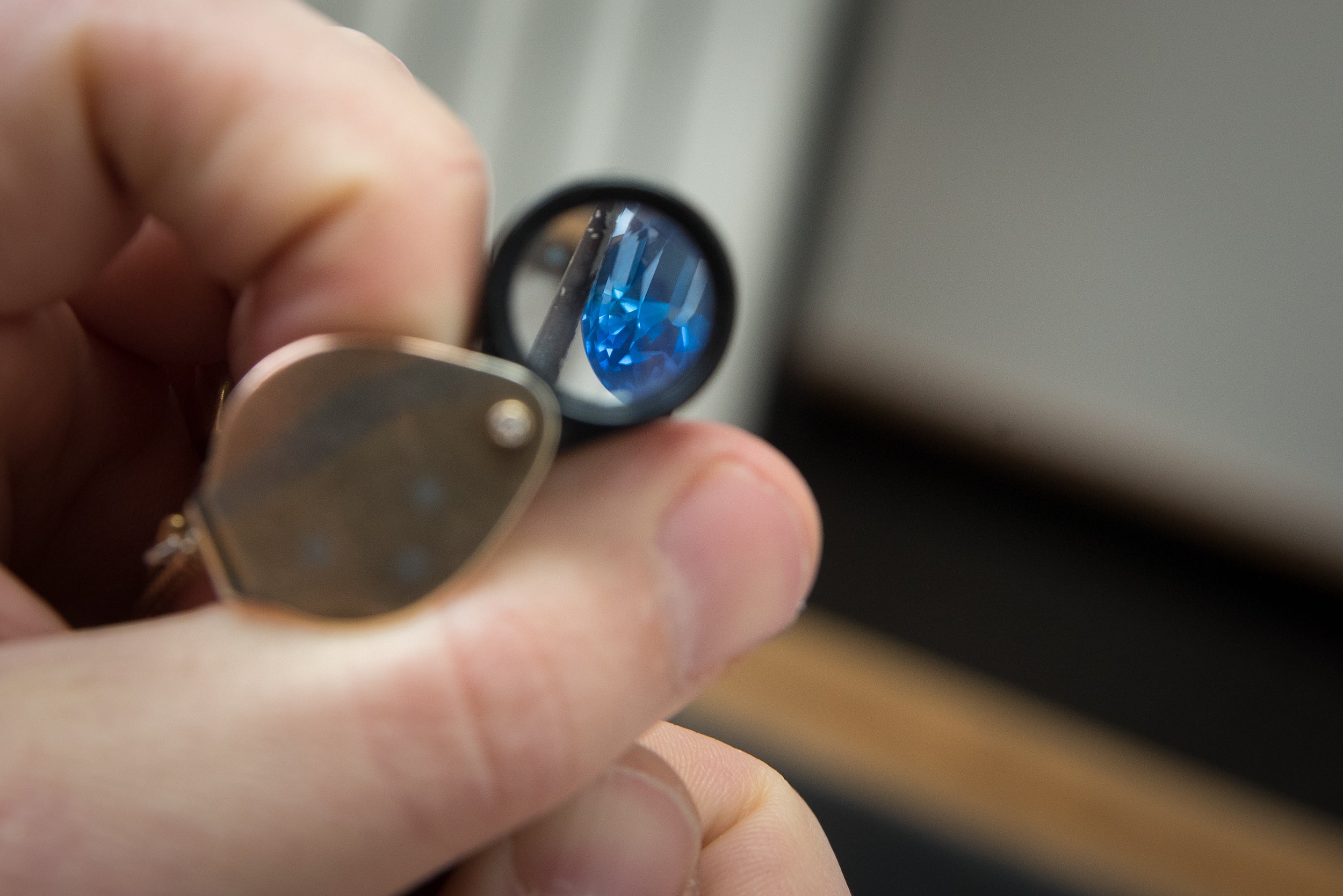 Close-up of a hand holding a blue sapphire in front of a jewelers loupe for an appraisal
