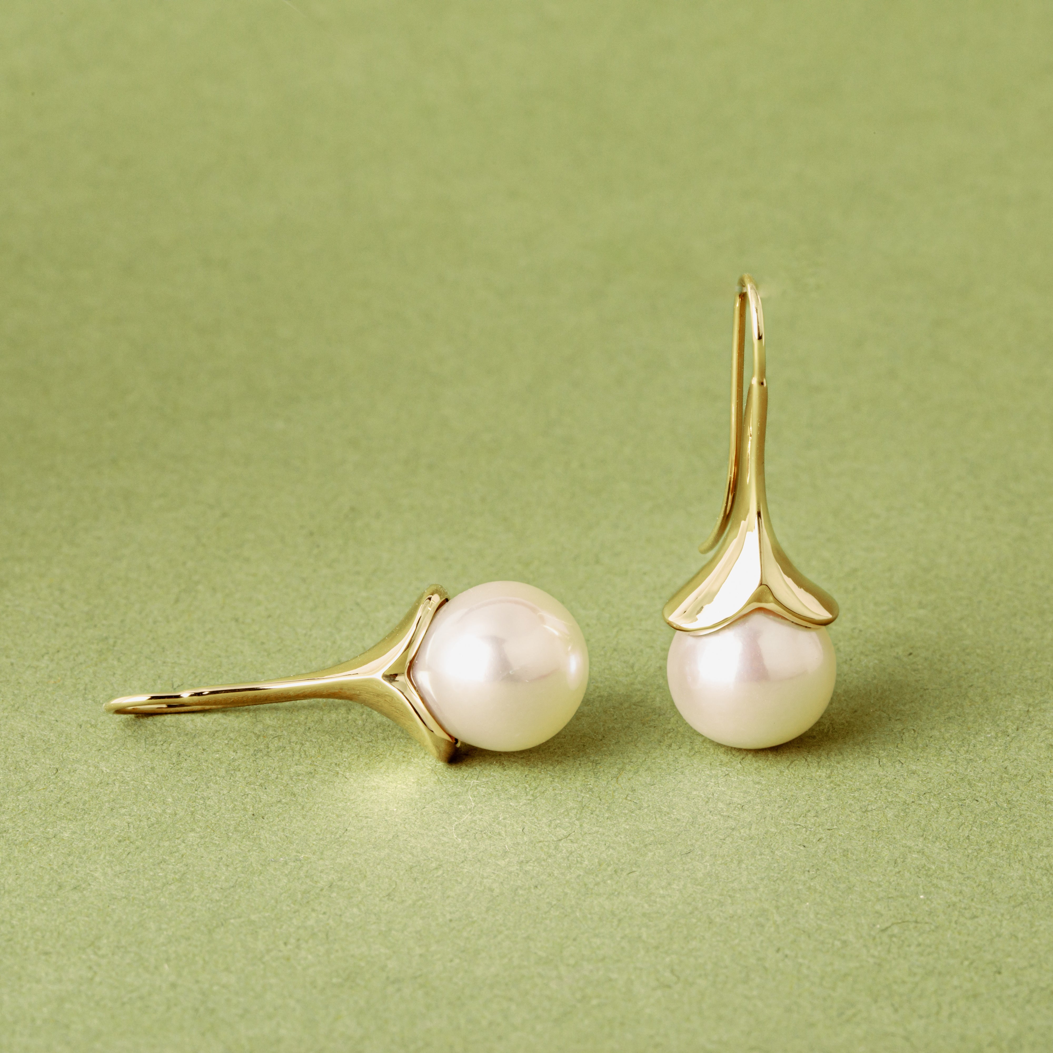 14k yellow gold lily-shaped drop earrings with large round white freshwater pearls on a sage green background, by deJonghe Original Jewelry