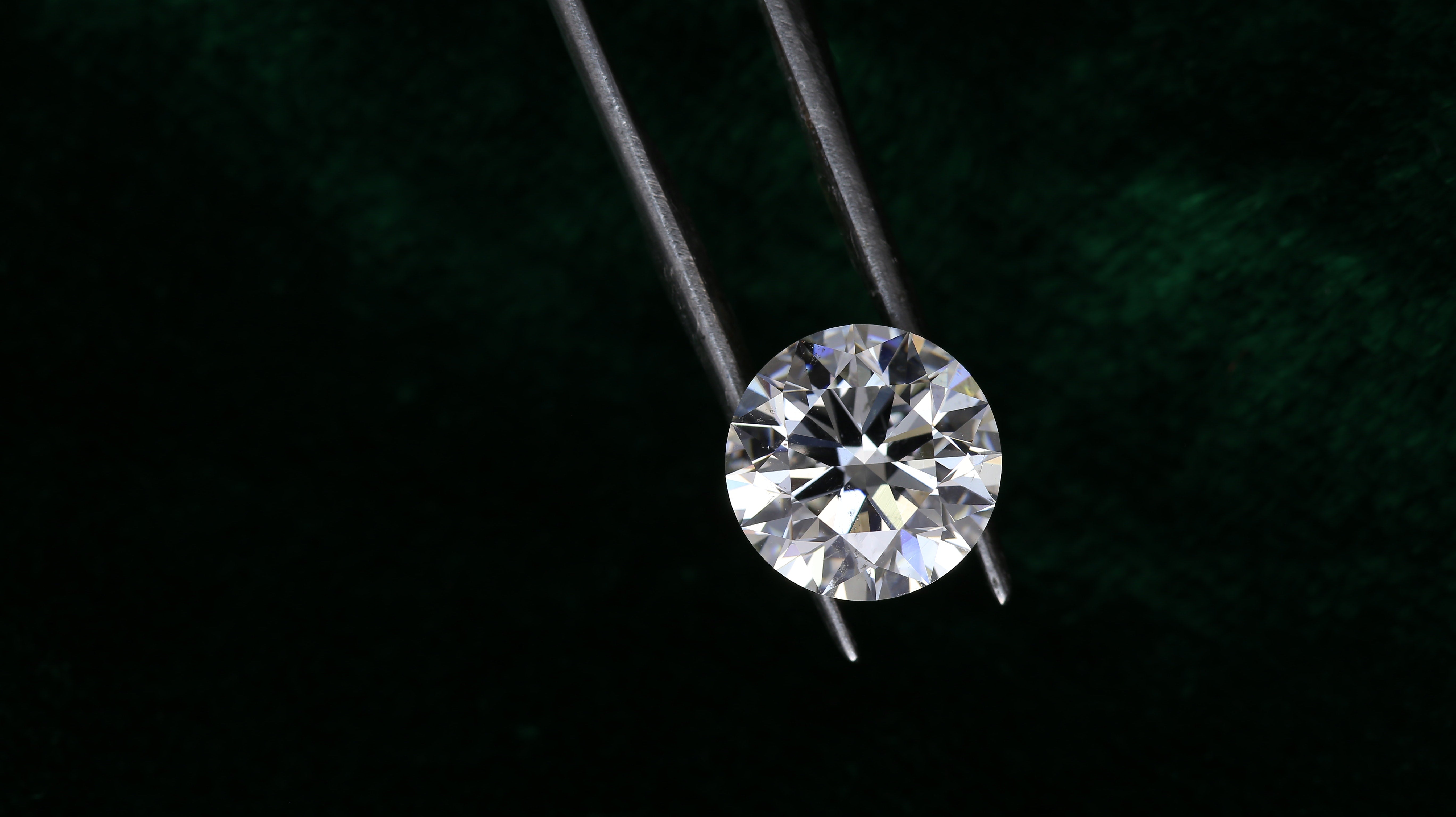 Diamond held by tweezers against a dark background