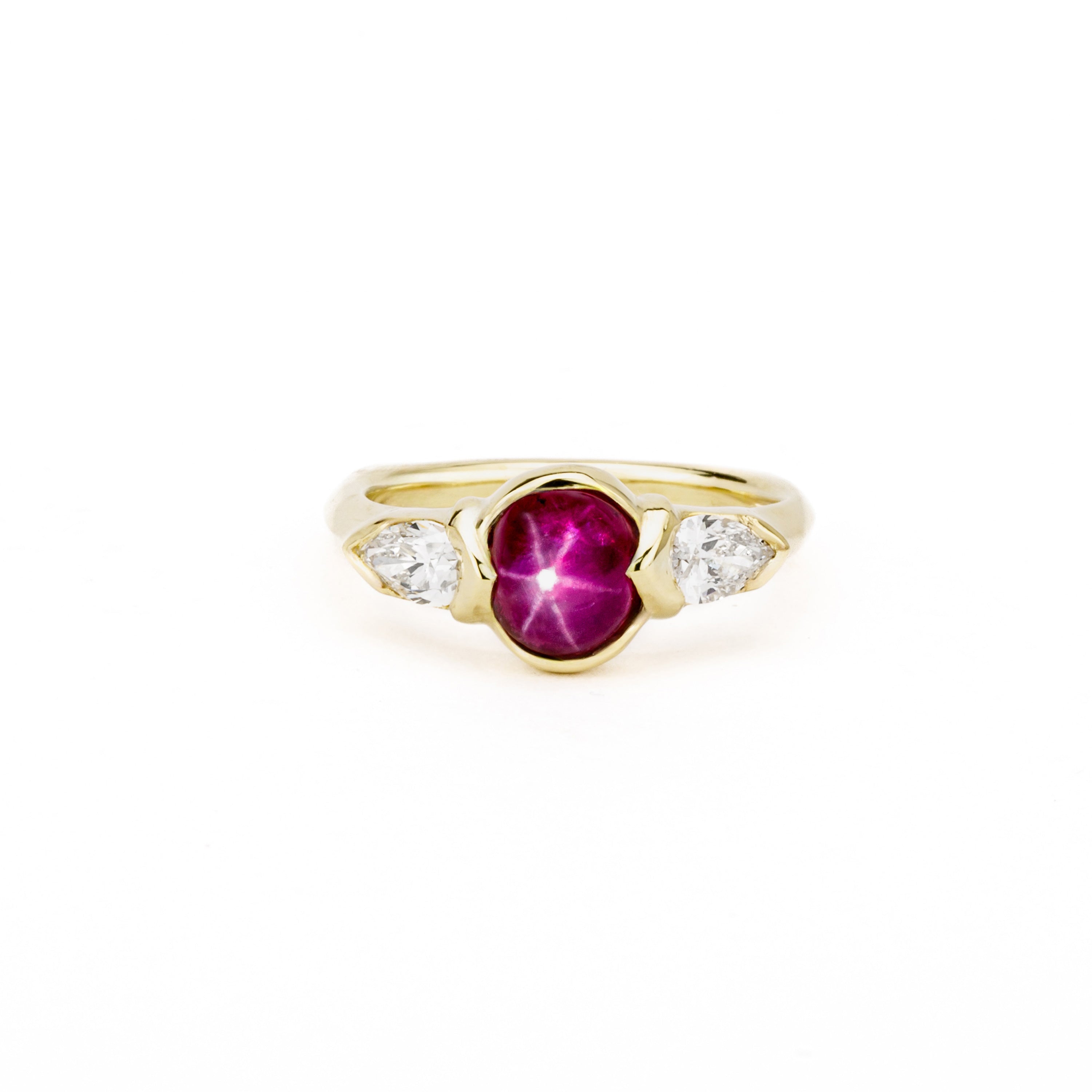 18k yellow gold three-stone ring featuring a 1.46ct star ruby cabochon with pear-shaped diamond accents